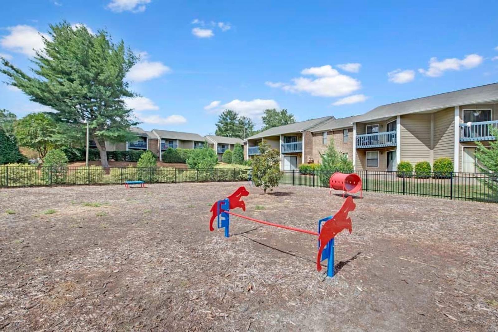 A small pet park featuring red horse-shaped seesaws and a fenced-in area with nearby apartments.