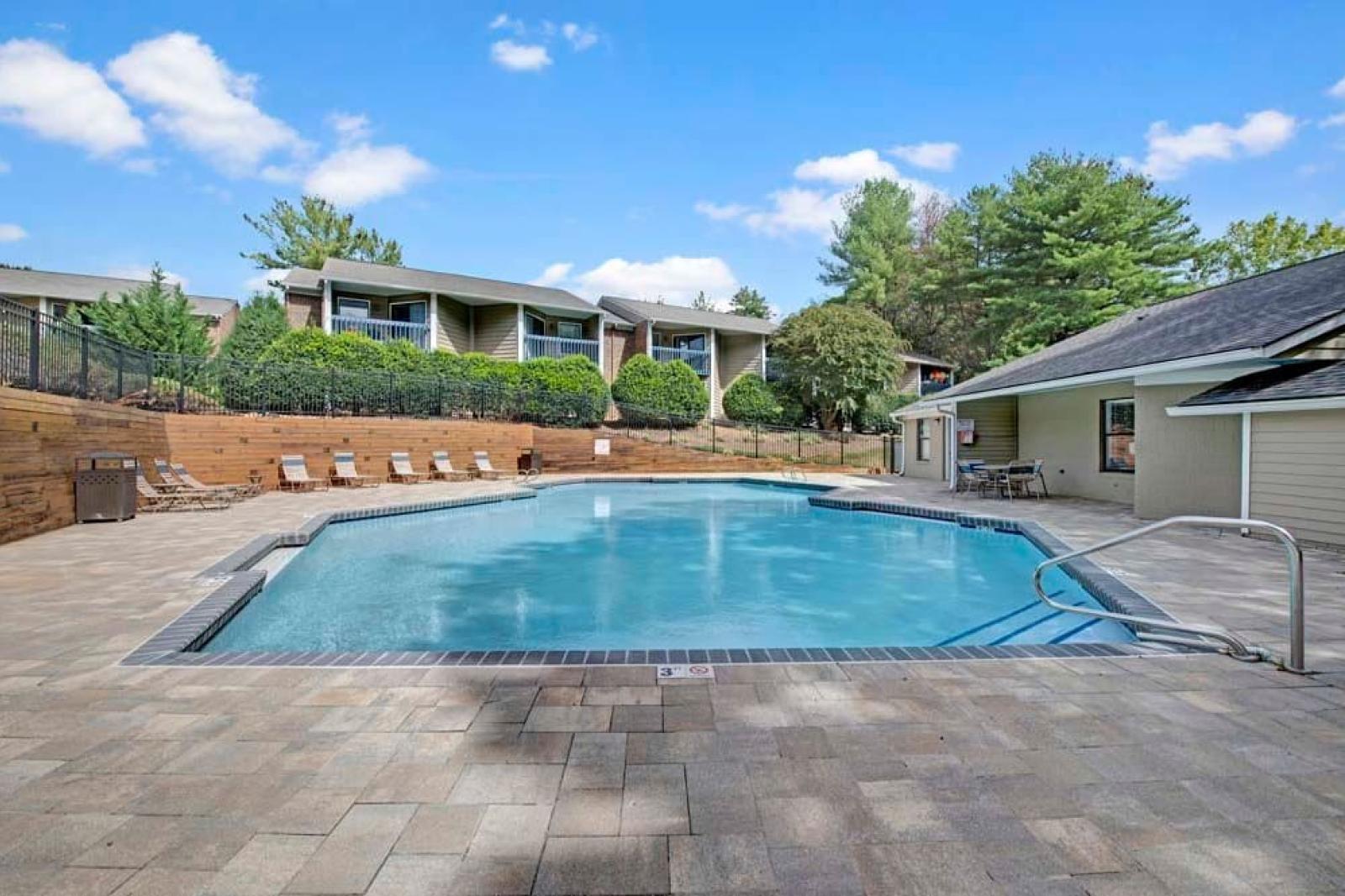 A crystal-clear swimming pool with paved surroundings and cozy seating, nestled among residential units.