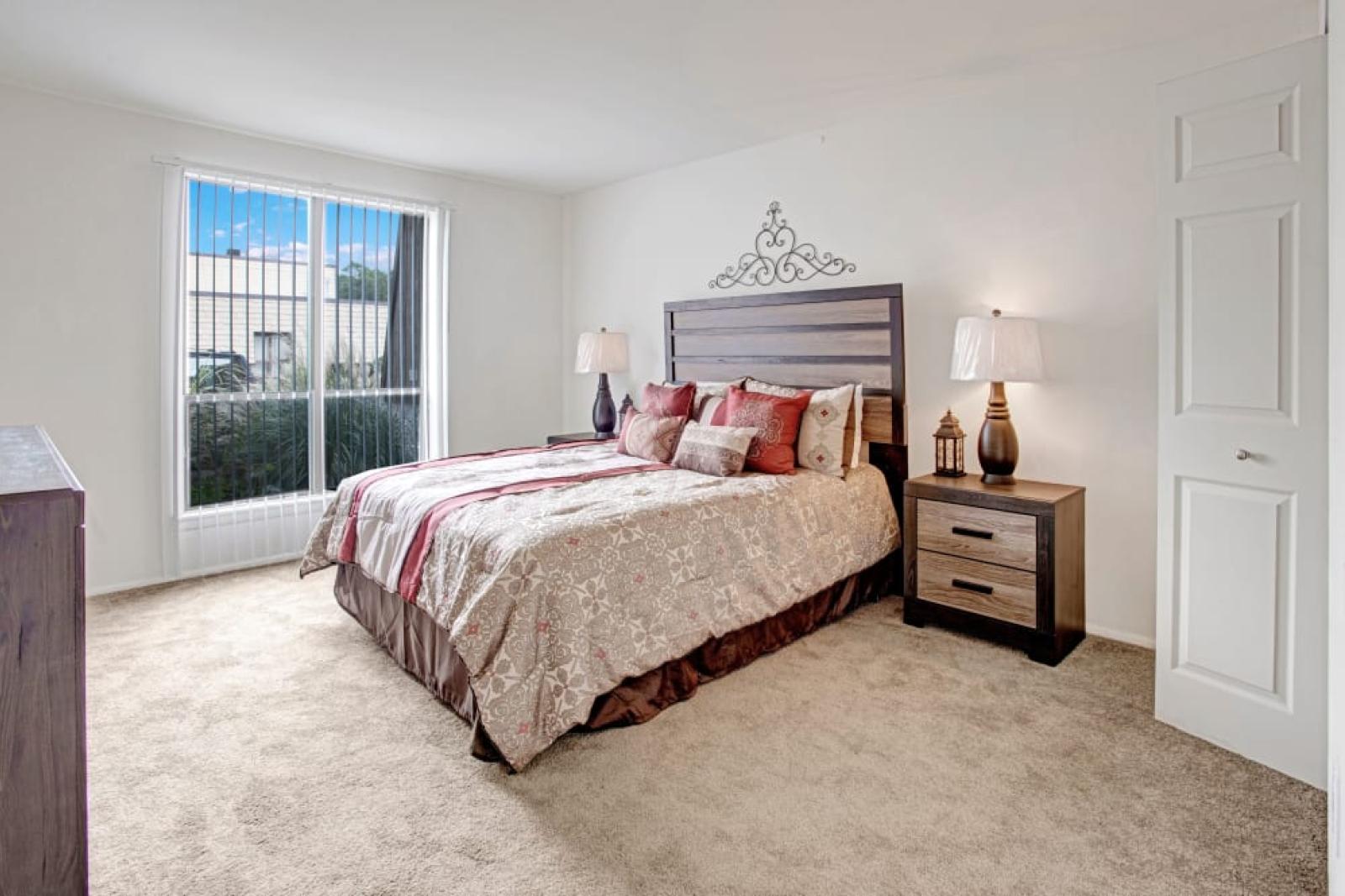 A serene bedroom with a large window, a patterned bedspread, and minimalist furniture.