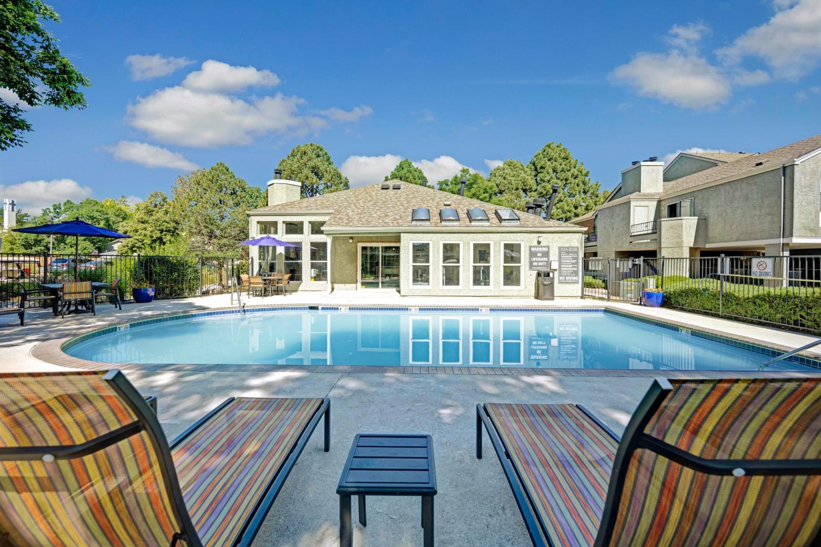 Relaxing pool area with colorful lounge chairs and umbrellas, offering a peaceful setting with a clear blue pool and a well-maintained clubhouse in the background at Waterfield Court Apartment Homes.