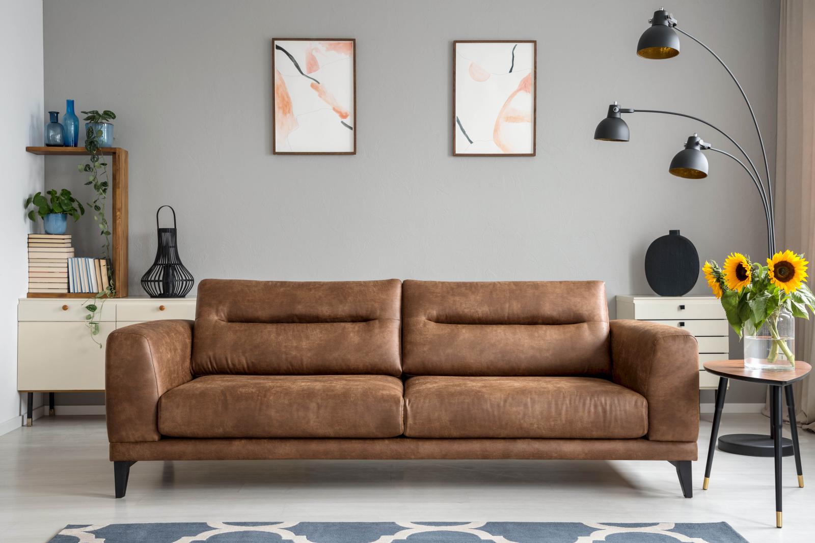 A stylish living room with a leather couch, modern decor, and vibrant sunflowers in a vase.