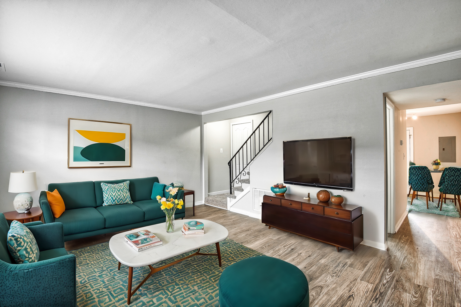 Fully staged living area at Maple Bay Apartments, featuring modern furniture, a mounted TV, and access to the dining area.