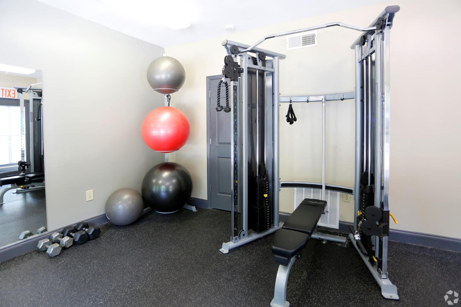 A fully equipped fitness center at Norcross Crossings Apartments featuring modern exercise machines, free weights, and yoga balls, with large windows providing natural light.