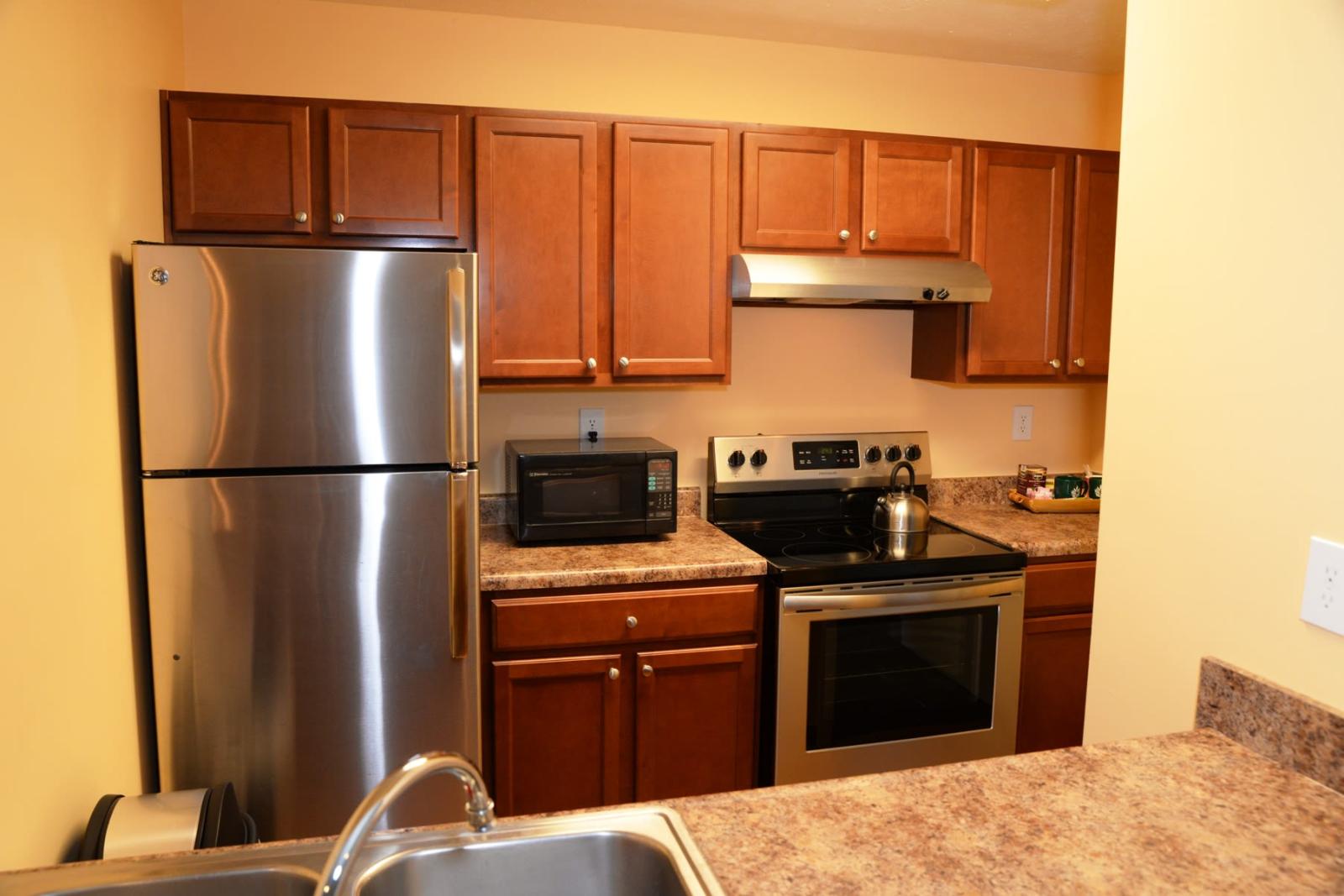 A modern kitchen at North River Place Apartments featuring stainless steel appliances, wooden cabinetry, and a polished countertop