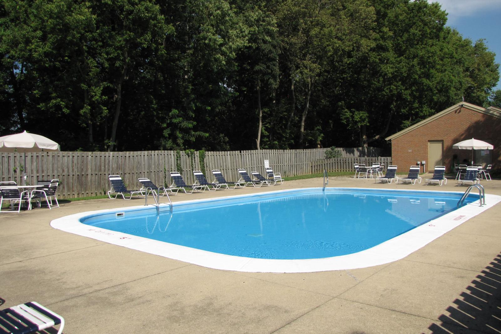 The outdoor pool area at North River Place Apartments, surrounded by lounge chairs, fencing, and trees, offers a refreshing retreat for residents