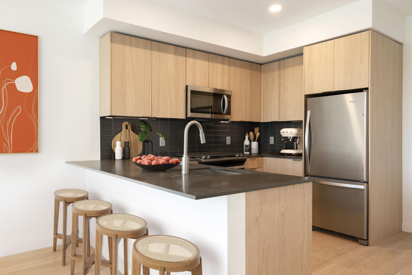 Modern kitchen featuring stainless steel appliances, wood cabinetry, and a sleek tile backsplash at The Edmund Apartments.