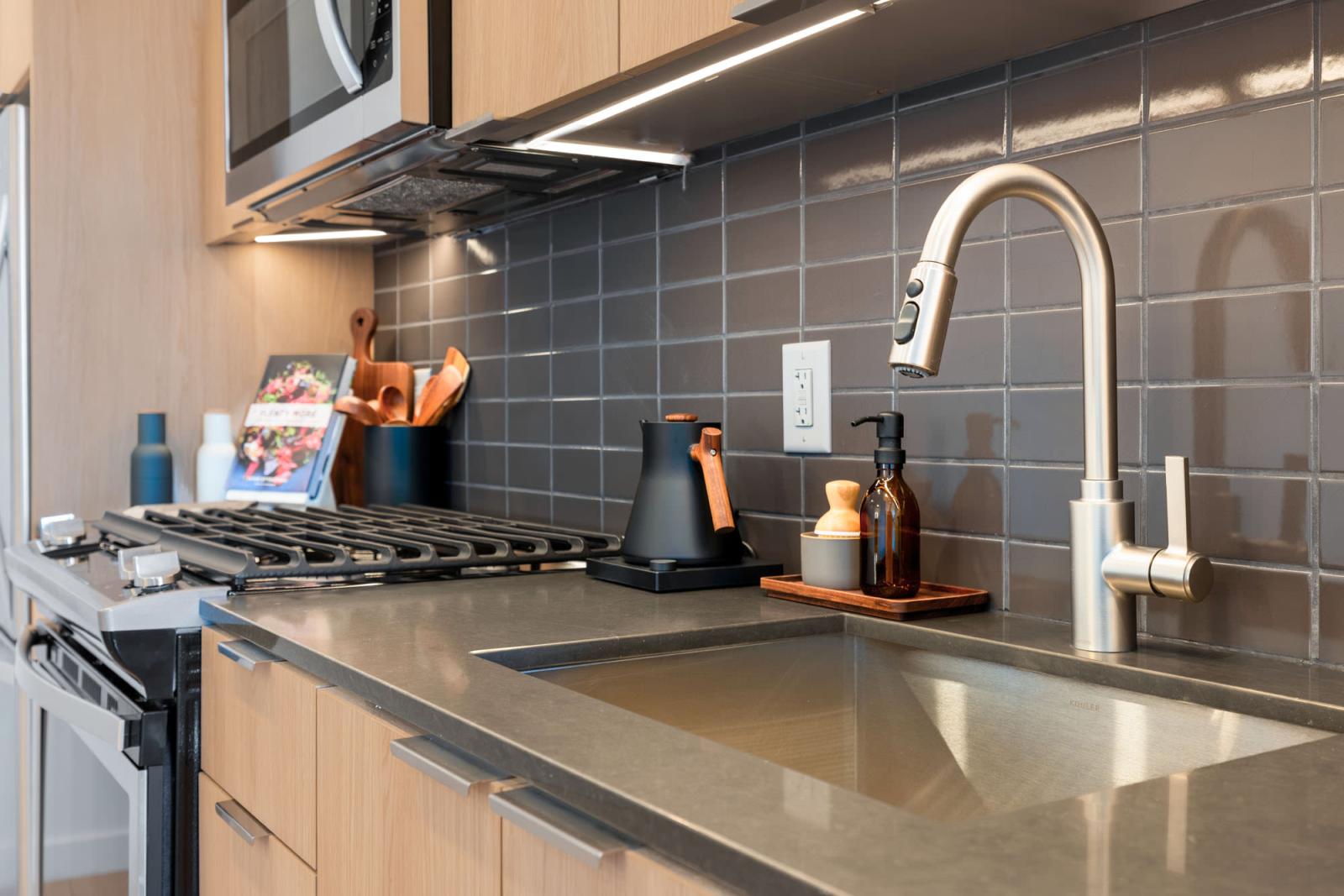 Modern kitchen featuring stainless steel appliances, wood cabinetry, and a sleek tile backsplash at The Edmund Apartments.