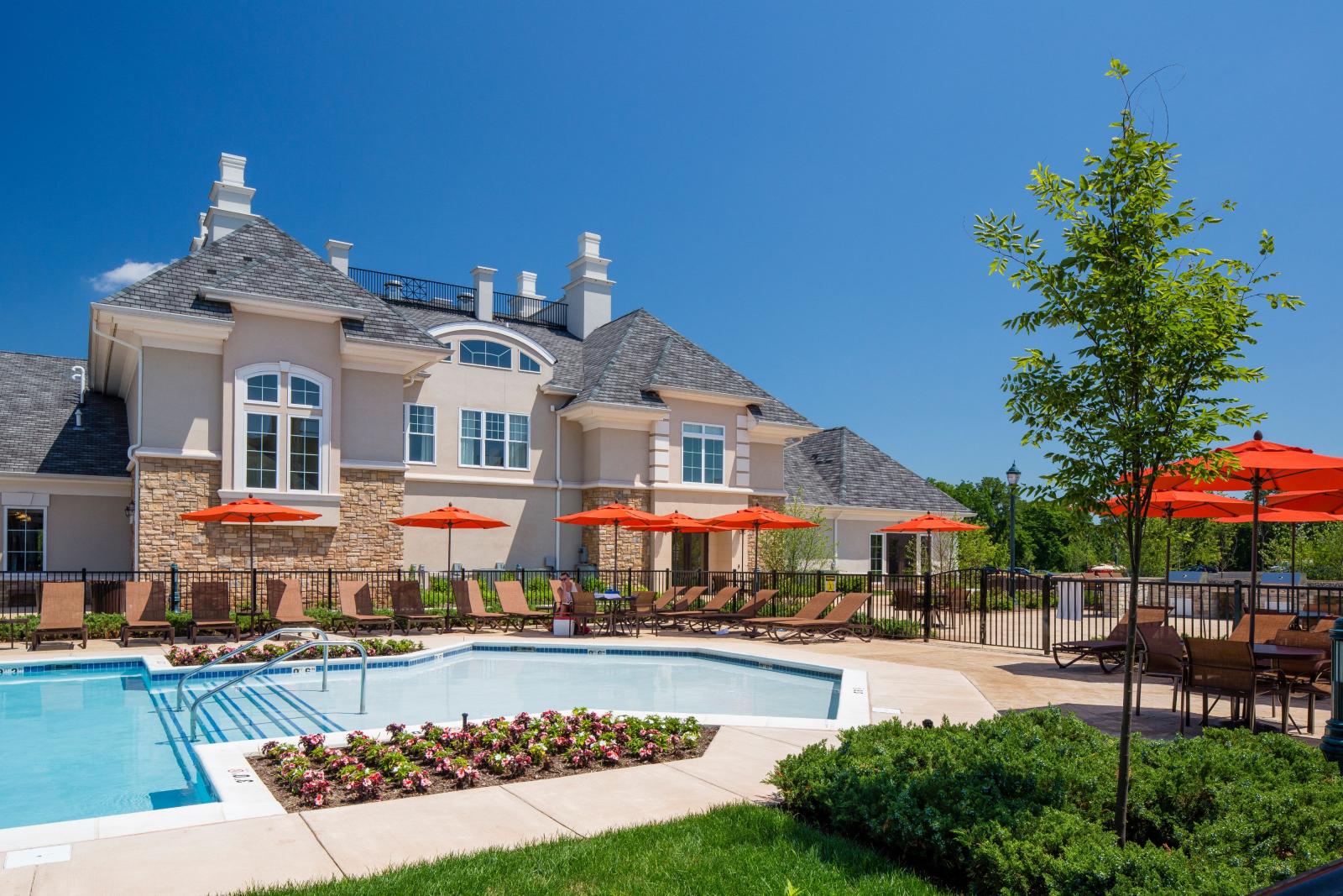 A vibrant outdoor pool area at The Grove Somerset Apartments, featuring cozy lounge chairs, bright orange umbrellas, and a beautifully landscaped backdrop.