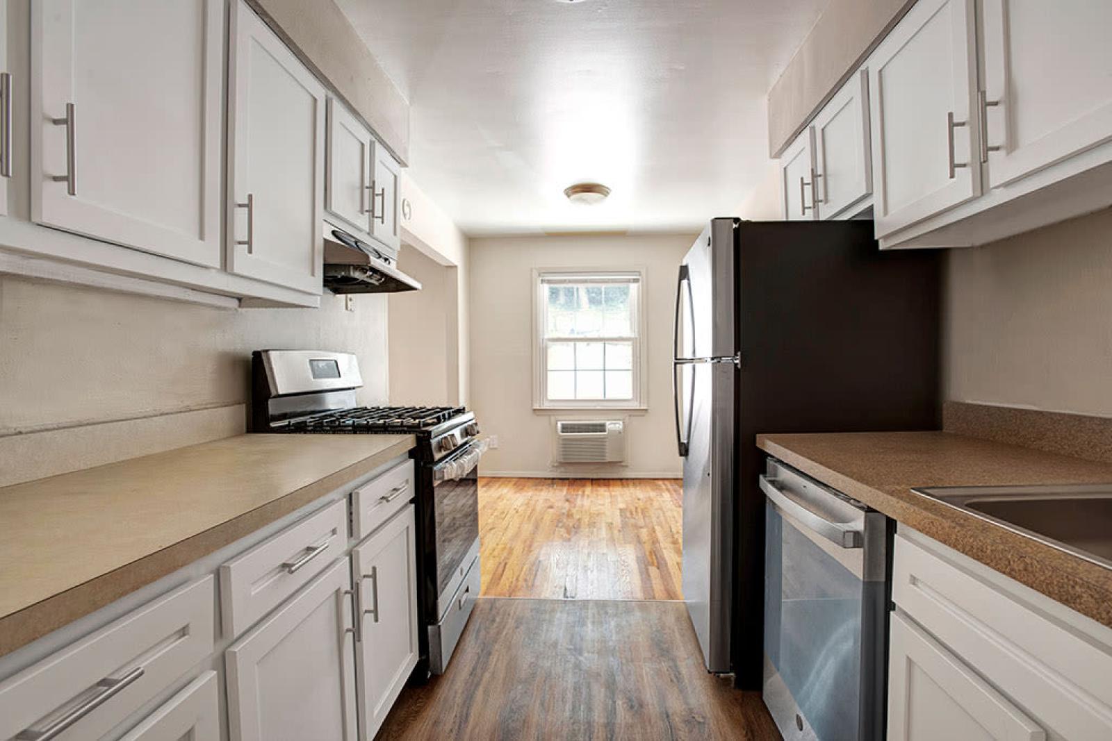 Modern galley kitchen with white cabinetry, stainless steel appliances, and natural light flowing in through a window, showcasing a cozy and functional layout.