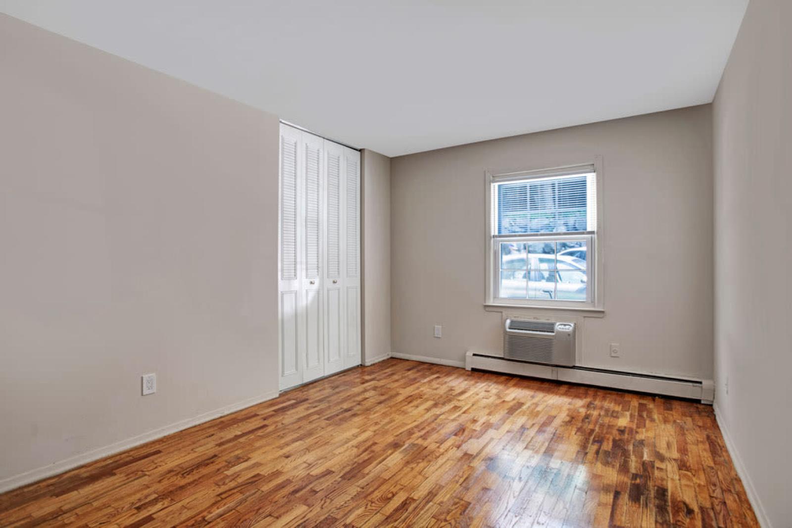 Bright bedroom with hardwood flooring, a large window for natural light, and ample closet space, ideal for restful nights.