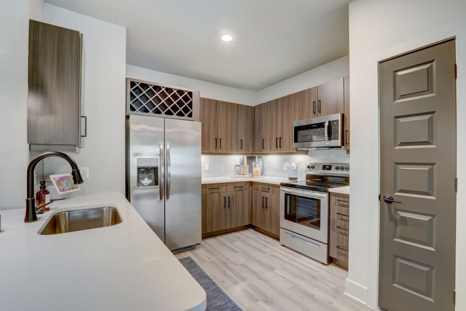 A fully equipped kitchen with sleek cabinetry, a wine rack, and stainless steel appliances in a Tropia Wellen Park apartment.