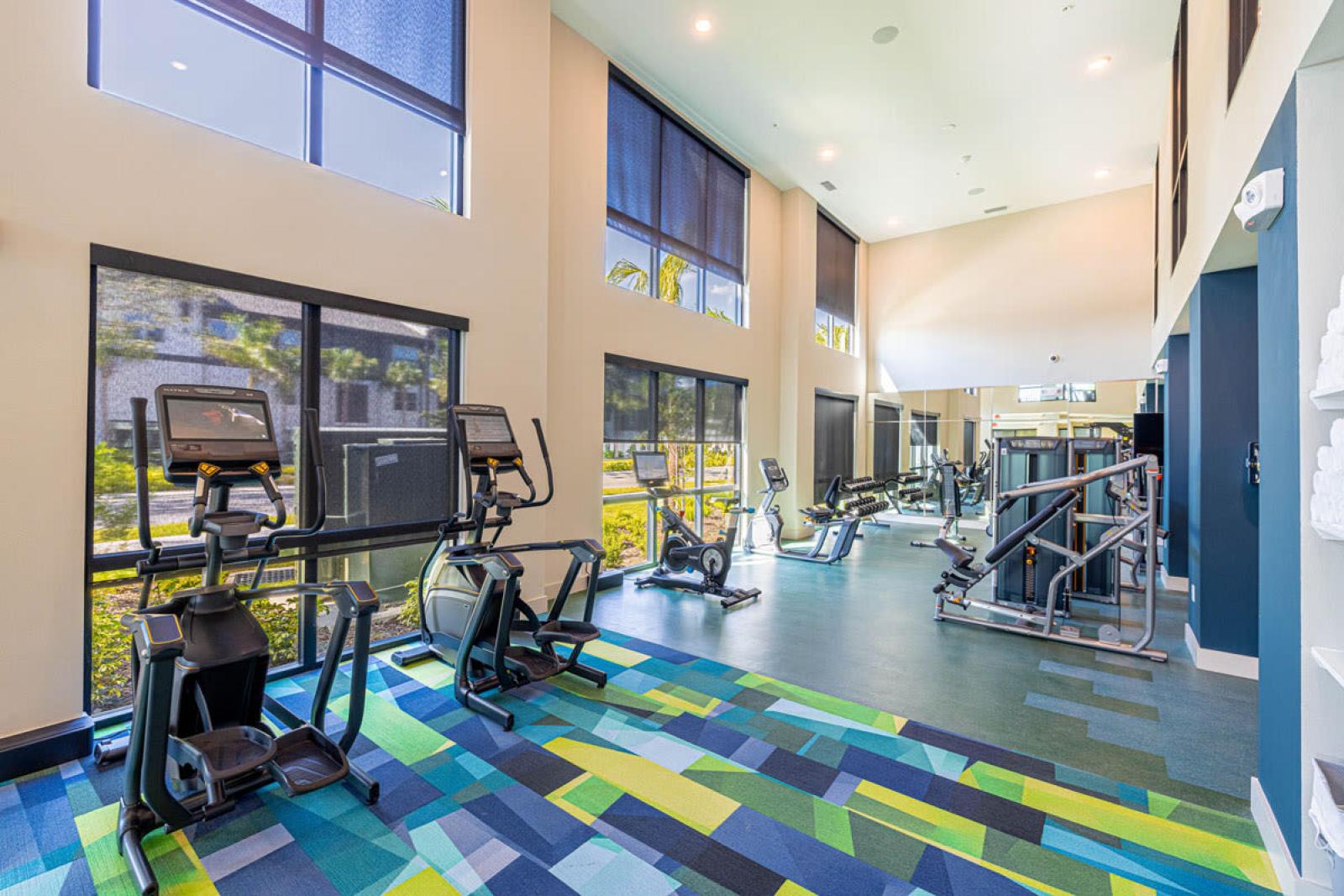 Image 1: Fitness center with modern exercise equipment, including a functional trainer, punching bag, and kettlebells, overlooking landscaped views through large windows.