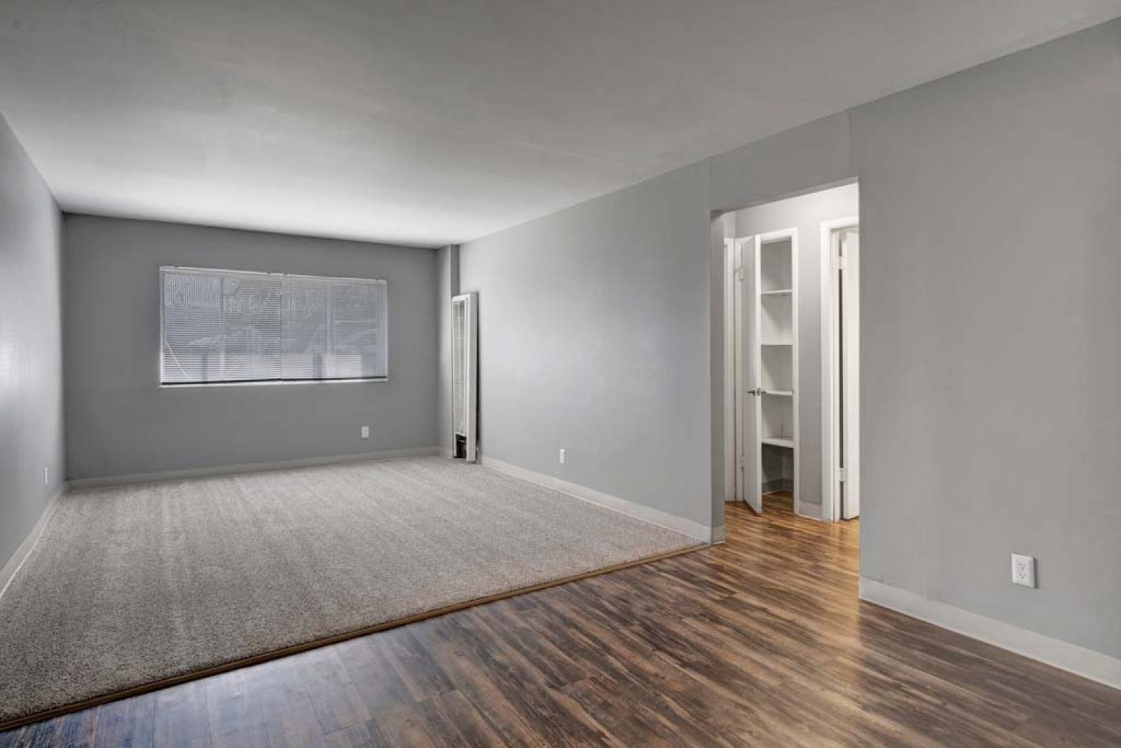 Spacious living room with a mix of carpet and hardwood flooring, featuring a large window that brings in natural light.
