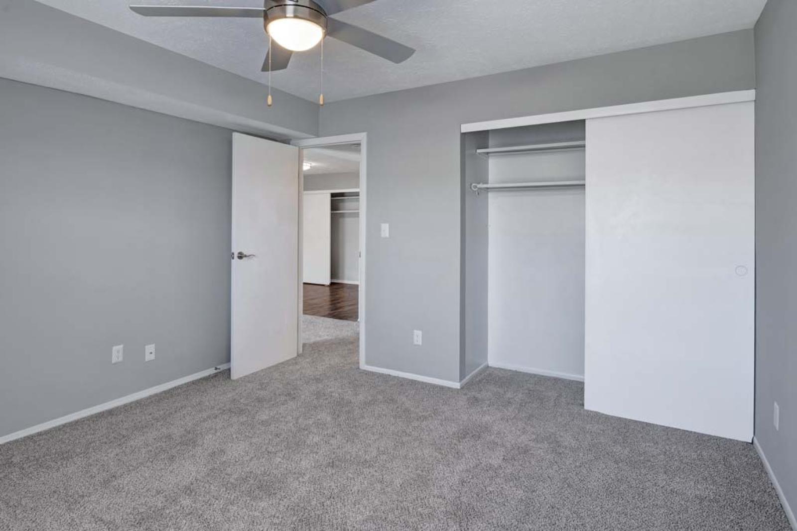 A cozy bedroom in a Wilson Plaza apartment featuring neutral carpet, a ceiling fan, and a spacious closet.