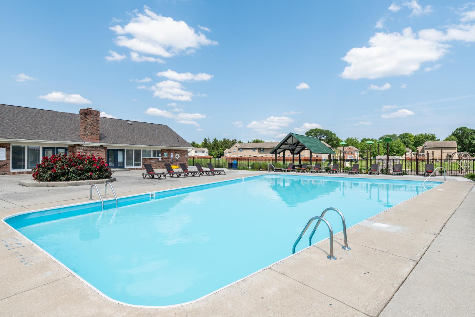 Outdoor swimming pool at Worthington Meadows Apartments with surrounding lounge chairs, a covered pavilion, and a landscaped community backdrop.