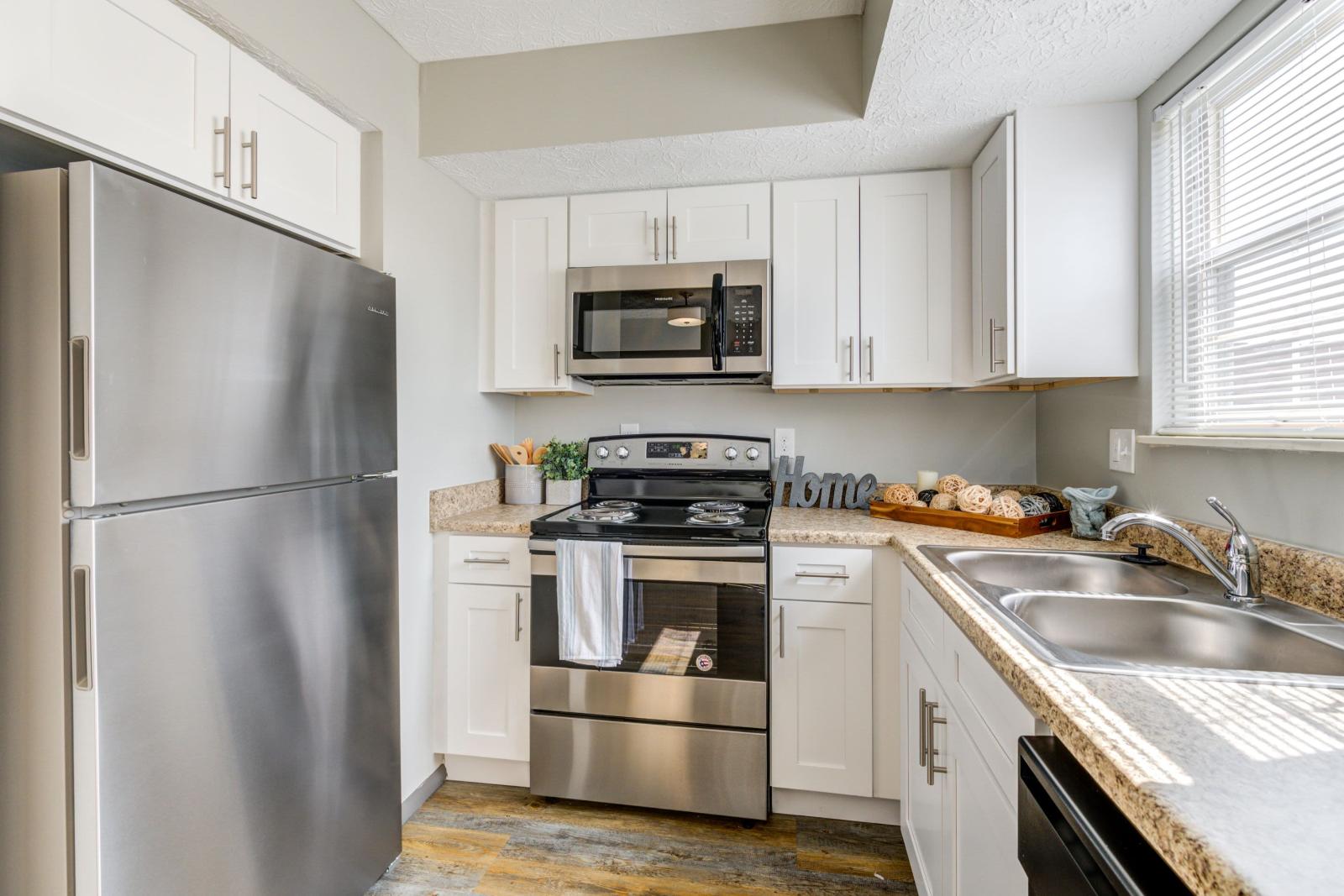 Fully equipped kitchen featuring stainless steel appliances, white cabinetry, and ample countertop space in Worthington Meadows Apartments.