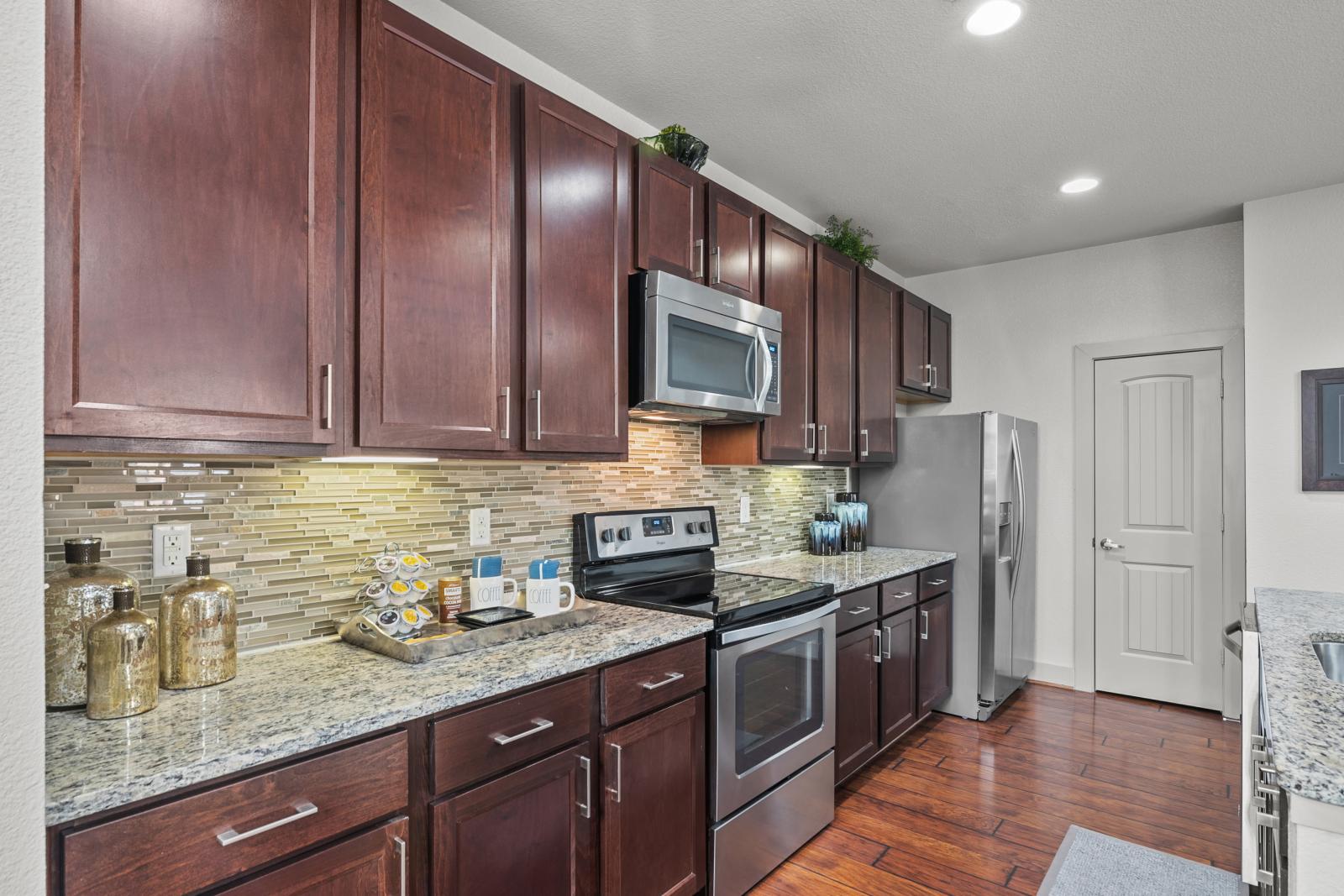A modern kitchen with granite countertops, stainless steel appliances, and a tile backsplash in a luxury apartment at Arrabella Apartments.