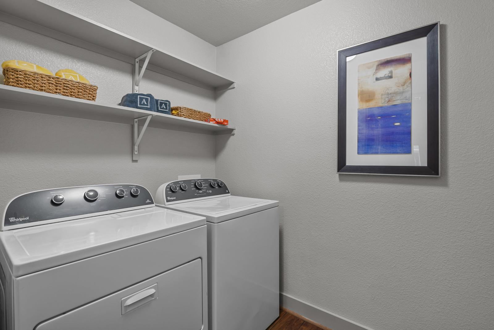 Spacious in-unit laundry room featuring modern Whirlpool washer and dryer with additional shelving for storage and organization.