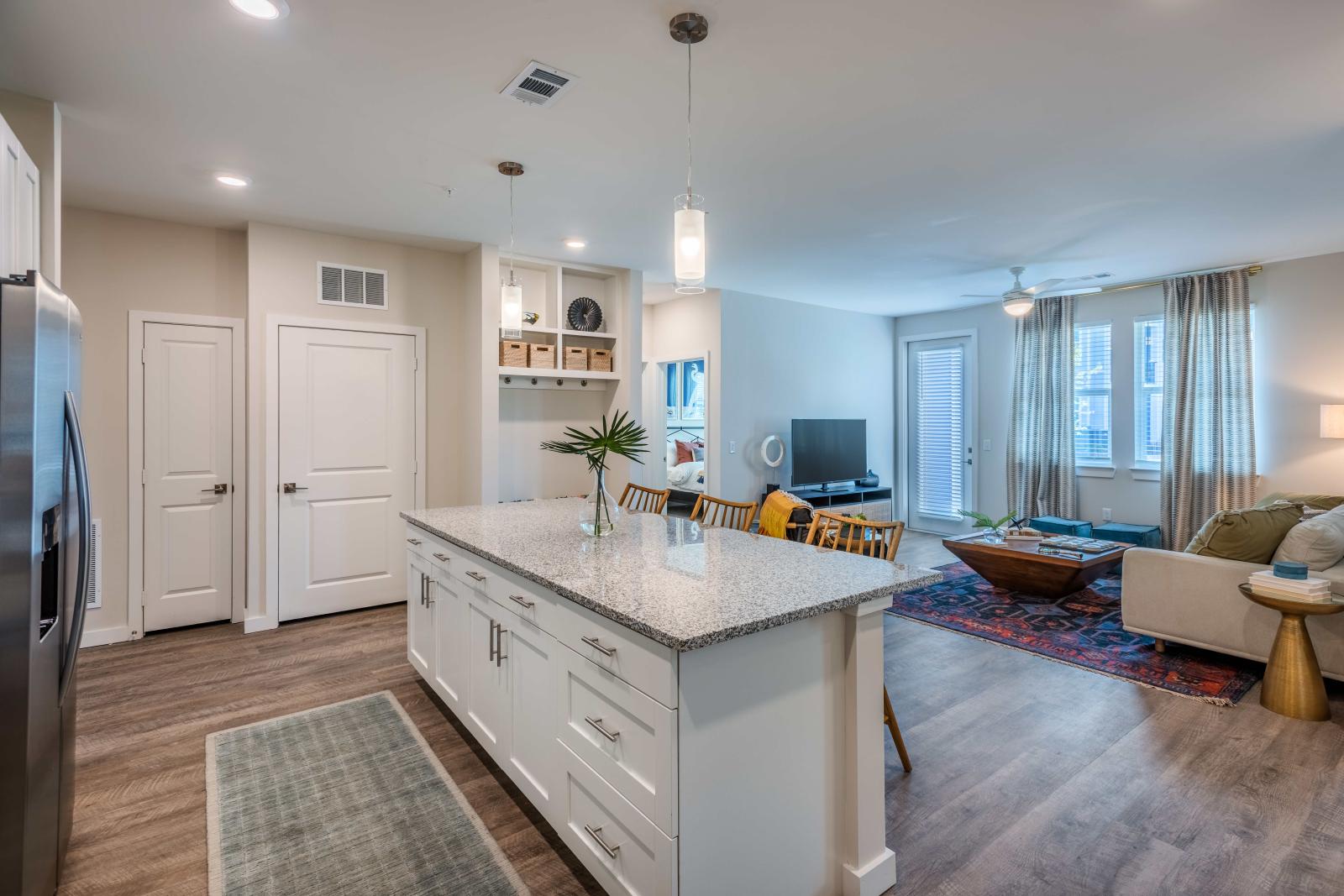 A modern kitchen featuring white cabinetry, stainless steel appliances, granite countertops, and pendant lighting over a spacious island with wooden barstools.