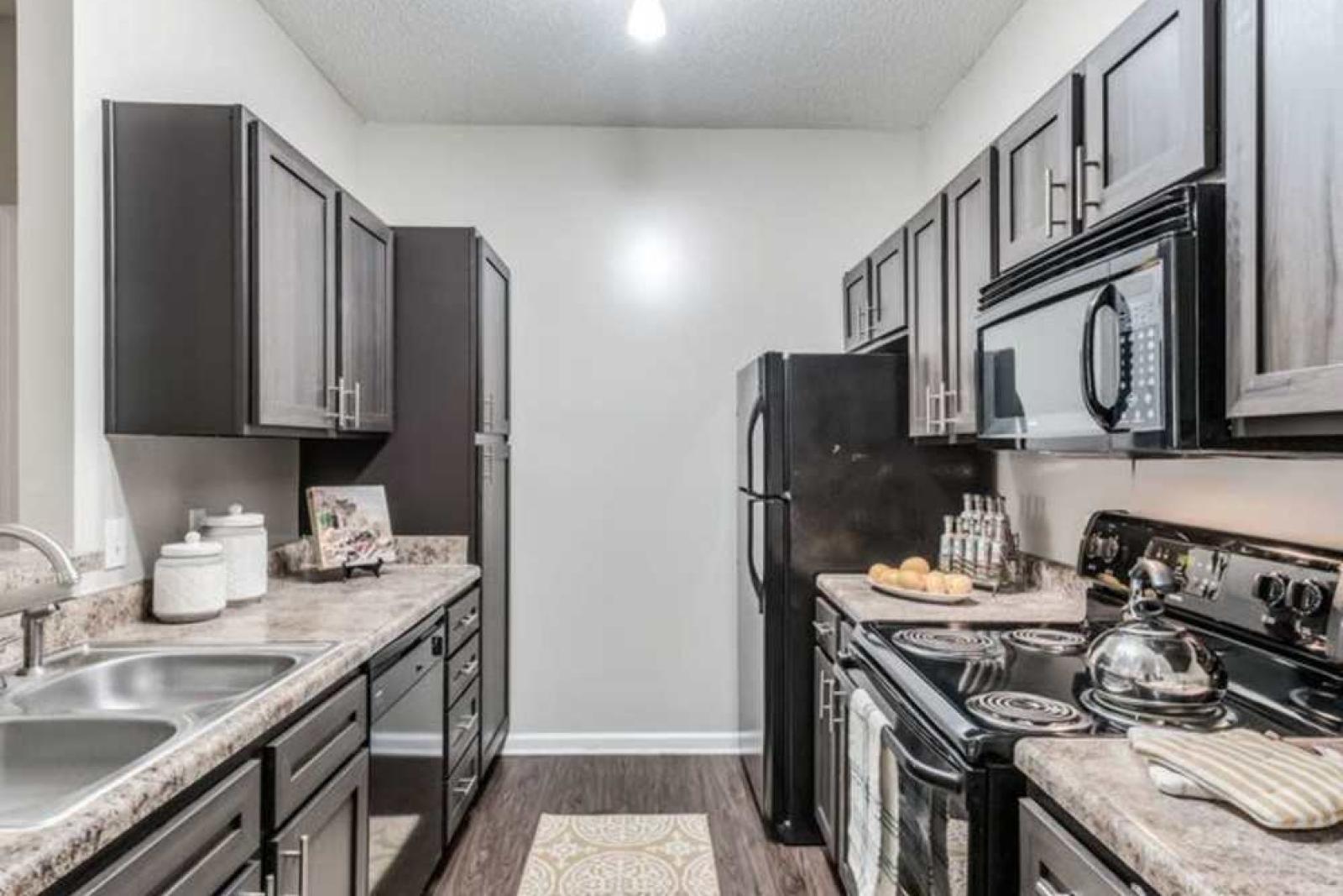 Modern kitchen with dark cabinetry, granite countertops, and stainless steel appliances at The Landings of Conroe Luxury Apartments.