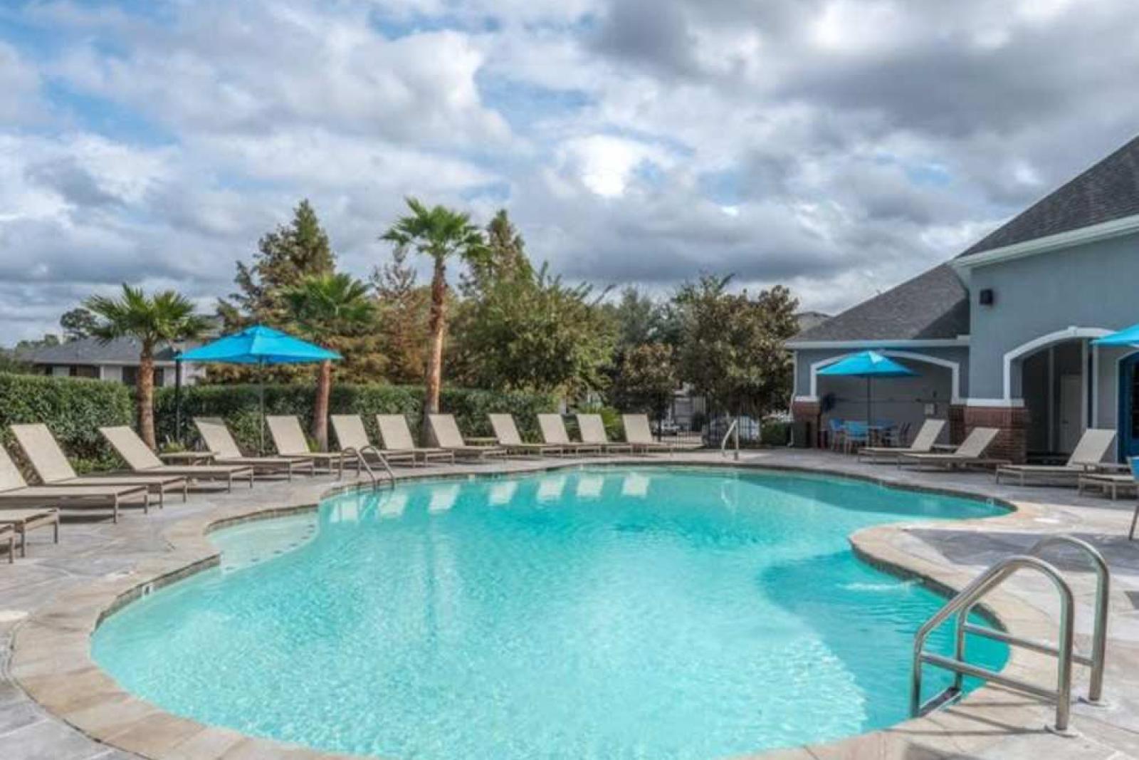 Sparkling blue pool with a stone-accented deck at The Landings of Conroe, featuring comfortable lounge chairs and shaded seating areas for relaxation.
