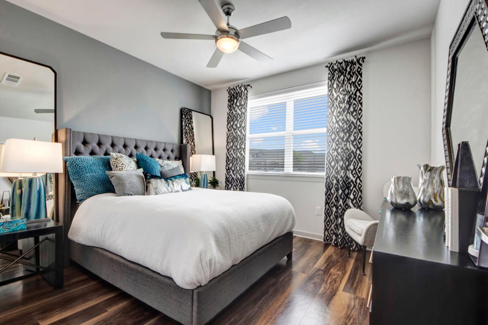 Elegant bedroom with a tufted gray headboard, cozy bedding, and a large window allowing natural light to brighten the space.
