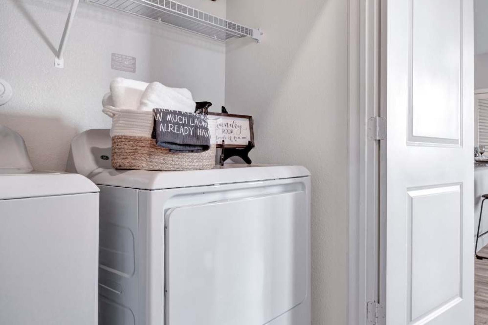 A well-organized laundry room with a washer and dryer, floating shelves, and charming decorative signs for a functional and stylish space.