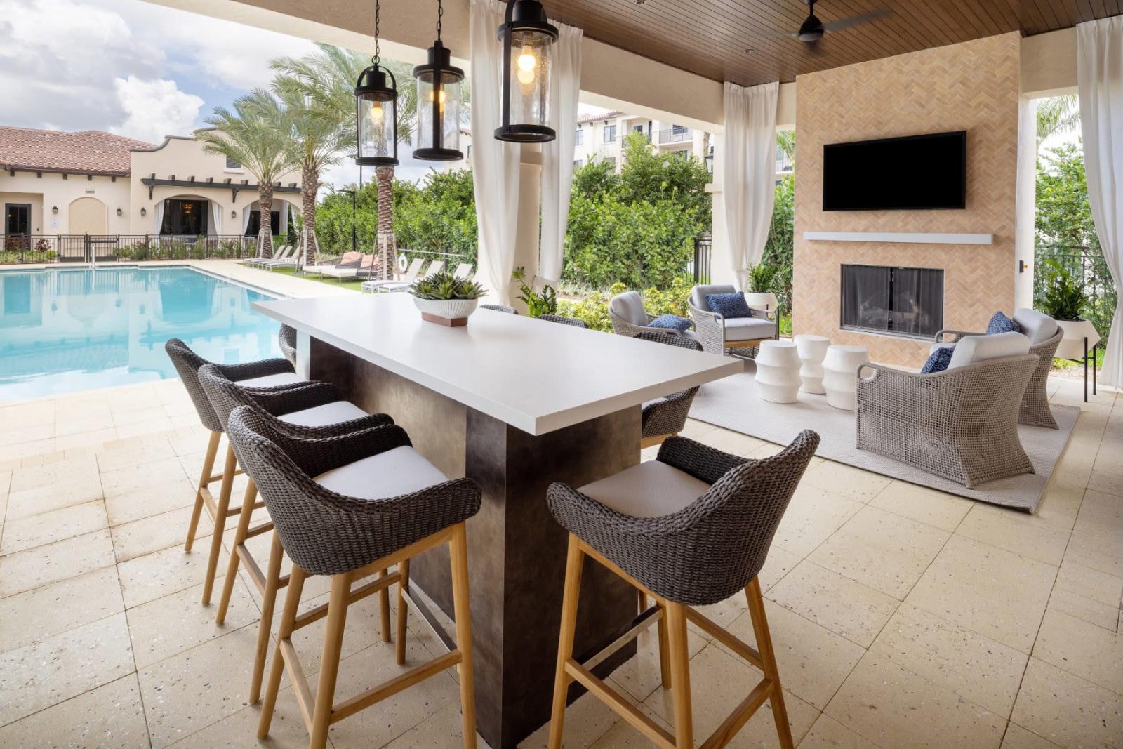 A modern outdoor bar with high-top seating and a cozy fireplace seating area, creating the ultimate entertainment space by the pool.