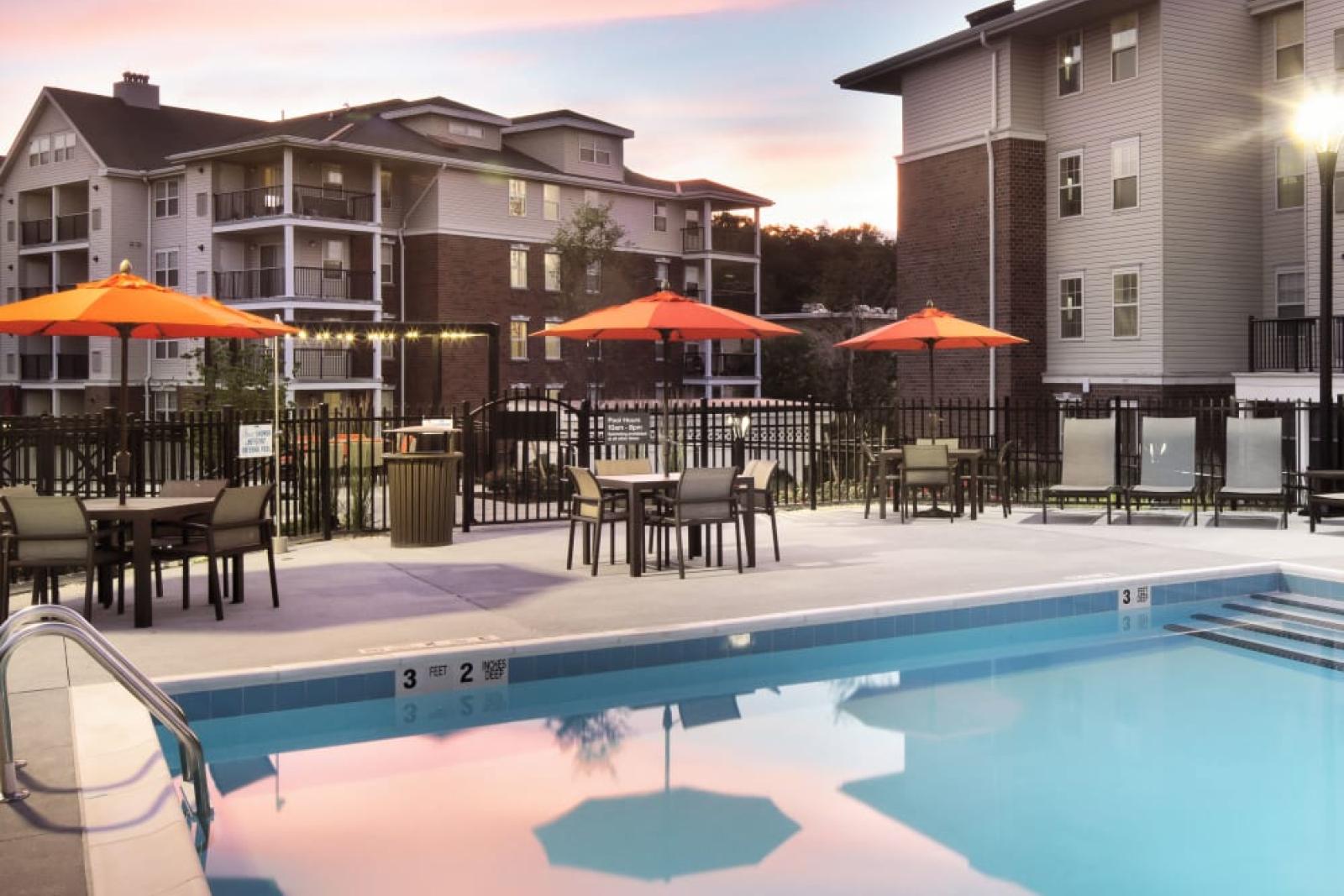 A stunning sunset over the pool area, reflecting soft colors in the water, with orange umbrellas and lounge chairs for relaxation.