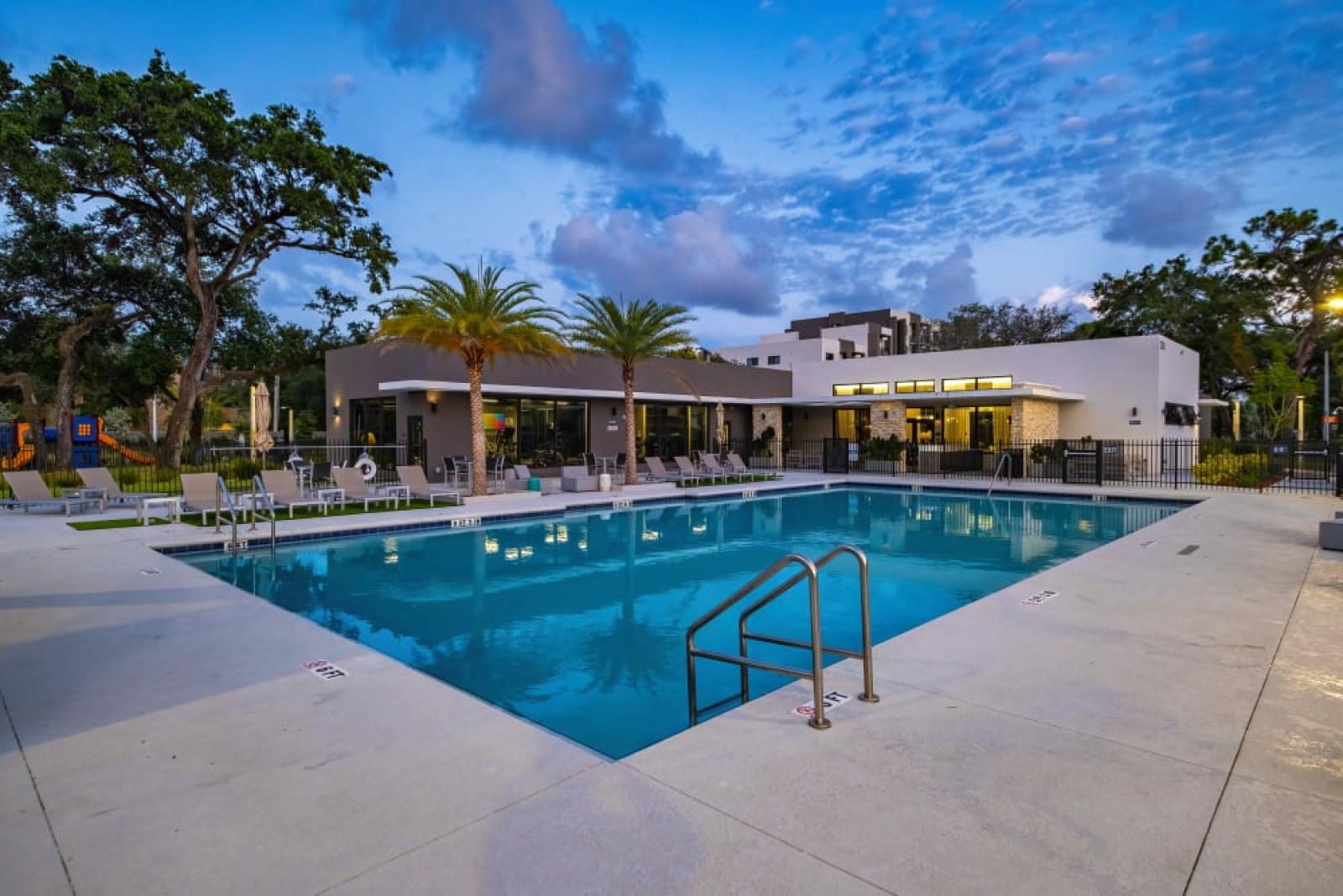 The pool at Oak Enclave illuminated at dusk, showcasing a peaceful and inviting atmosphere with warm lighting and stylish seating.
