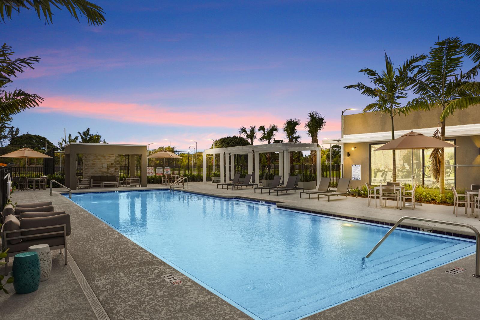A resort-style pool at sunset with poolside seating, cabanas, and lush palm trees, creating a tranquil retreat for residents.