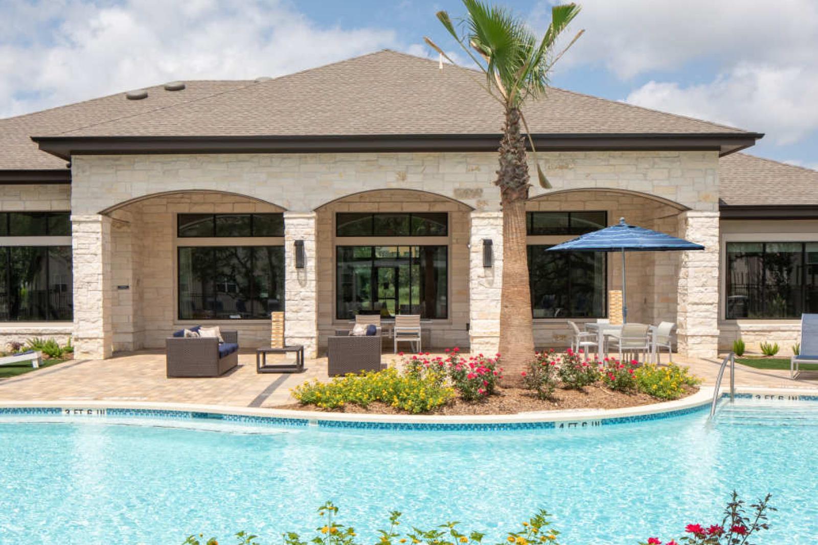 Clubhouse exterior at Vista At Town Green, featuring elegant stone architecture, large windows, and a beautifully landscaped pool area for residents to enjoy.