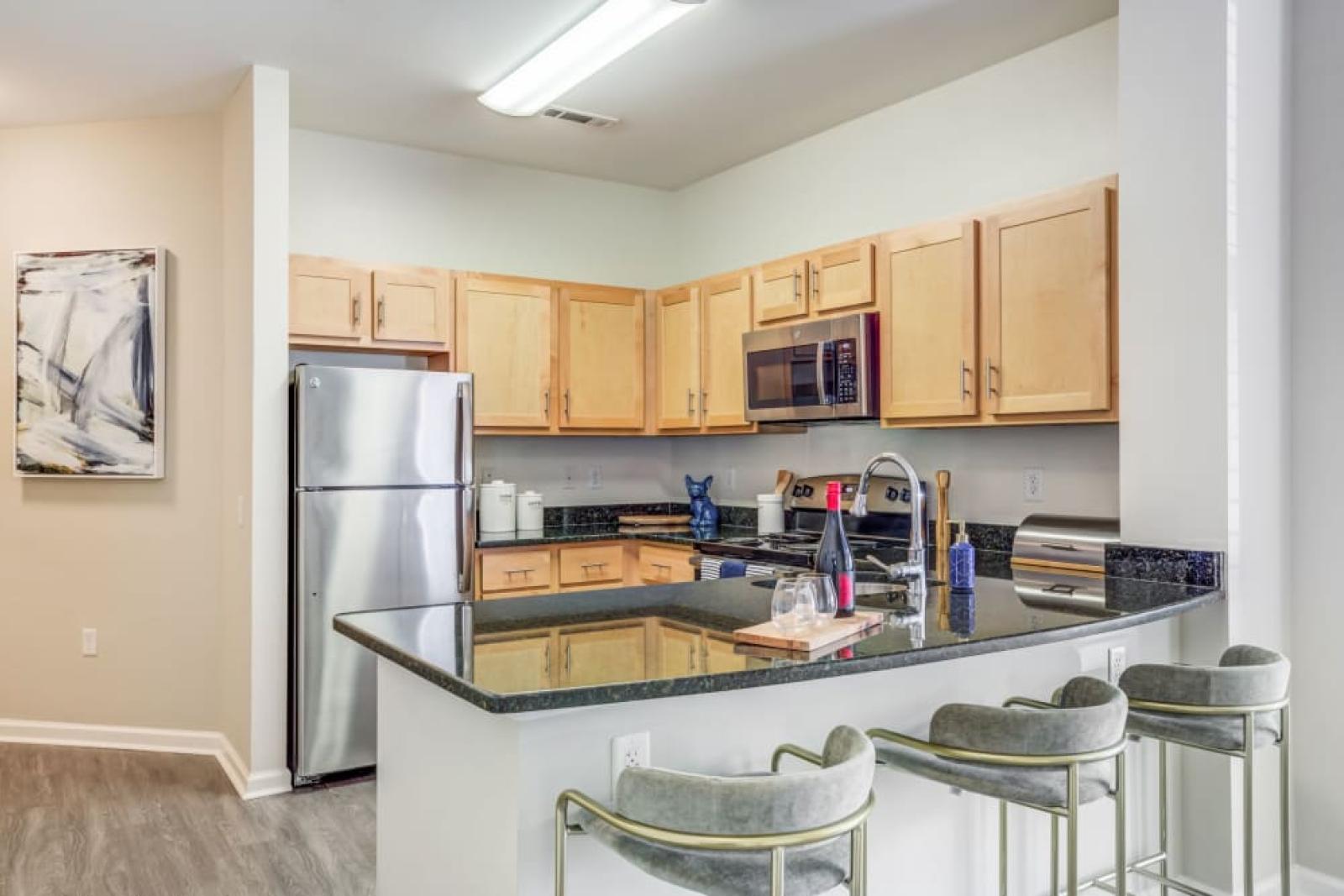 A stylish kitchen in an Oak Enclave apartment, showcasing stainless steel appliances, wooden cabinetry, and a sleek black granite countertop with bar seating.
