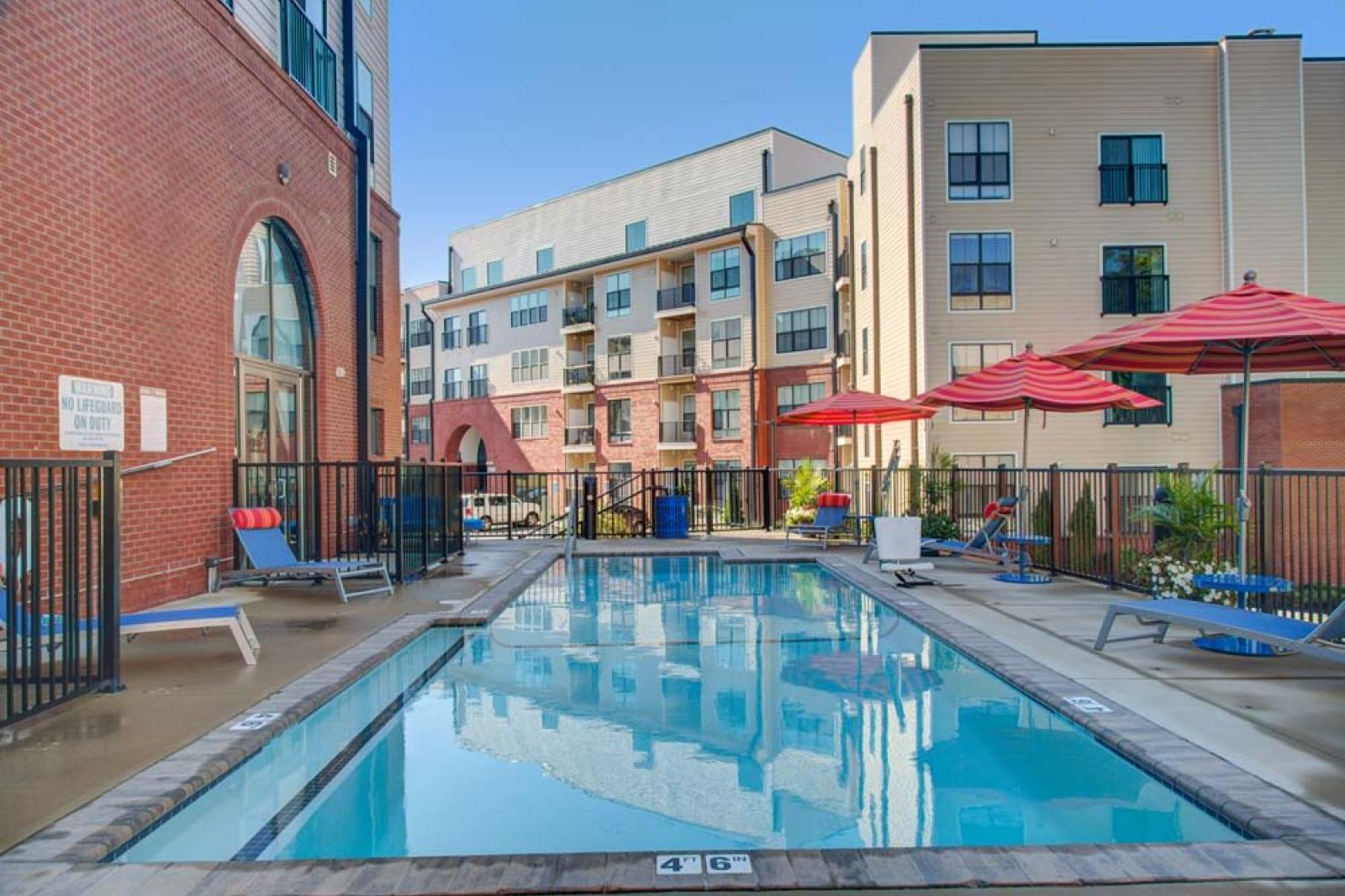 A closer view of the resort-style pool at The Royal Belmont, with red umbrellas, comfortable seating, and arched building entrances.