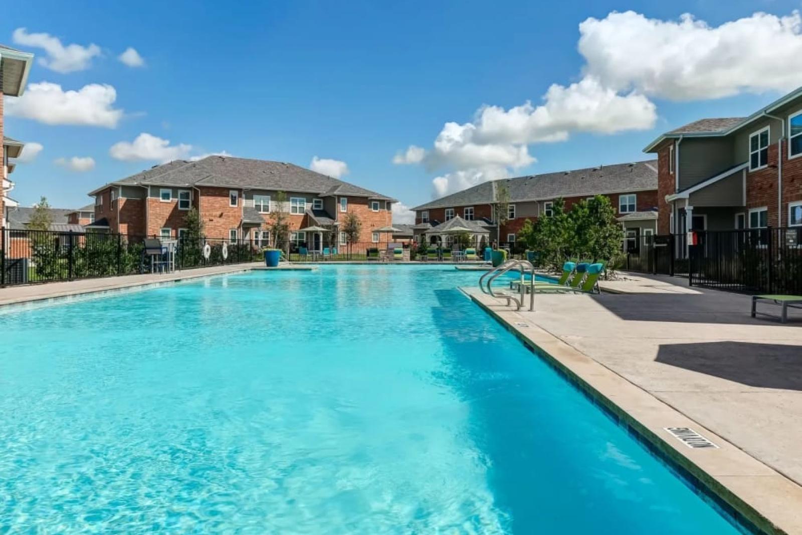 Expansive pool area with crystal-clear water and poolside seating at The Emerson at Forney Luxury Apartments, perfect for relaxation.