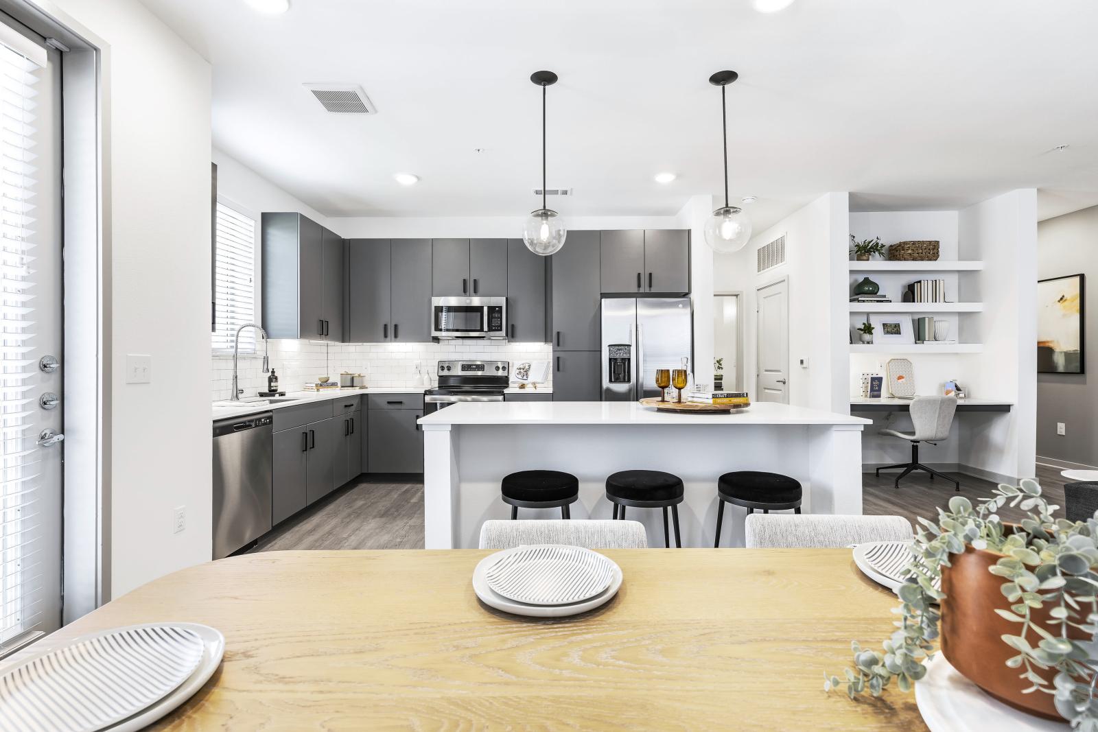 A stylish dining space with a wooden table set for a meal, seamlessly connected to a modern kitchen with pendant lighting and sleek finishes.
