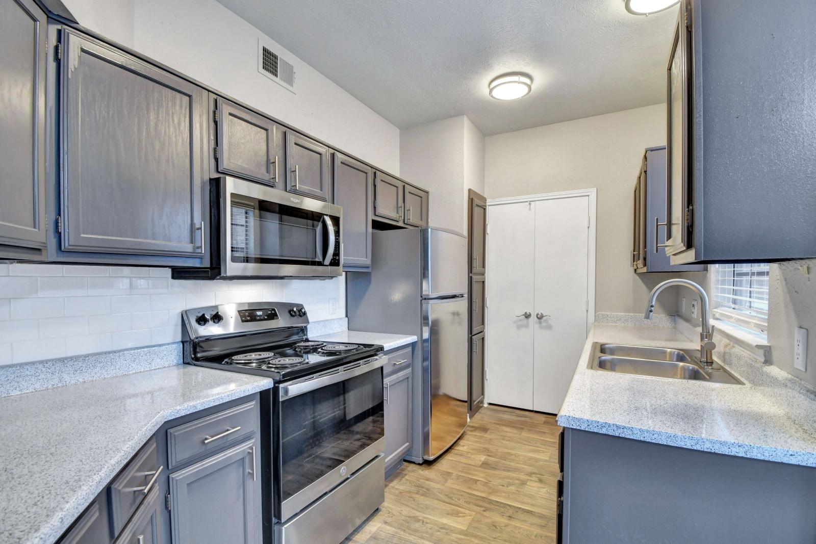 Modern kitchen with gray cabinetry, stainless steel appliances, granite-style countertops, and wood-style flooring.