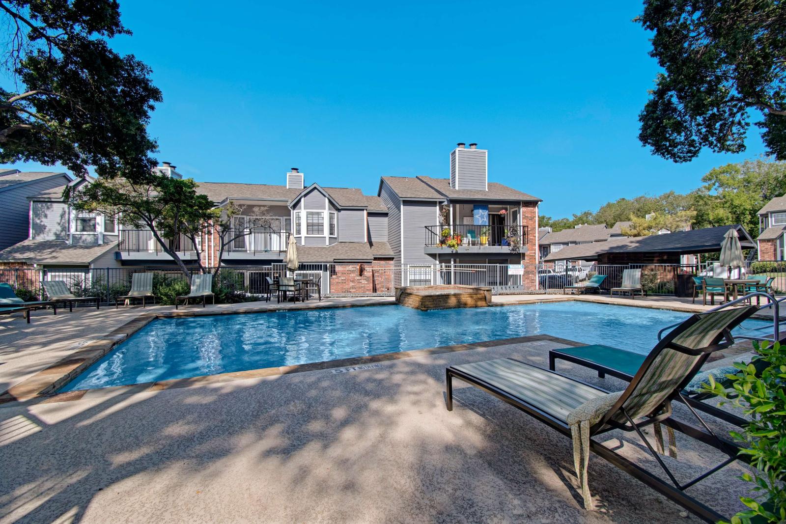 View of the community swimming pool with water feature, surrounded by lounge seating and multi-story residential buildings.