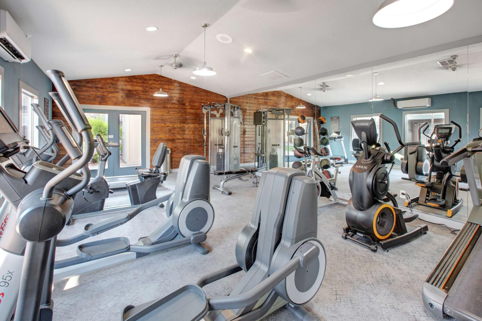 Fitness center with cardio and strength training equipment, including ellipticals, stationary bikes, and free weights, set against wood-accented and mirrored walls.