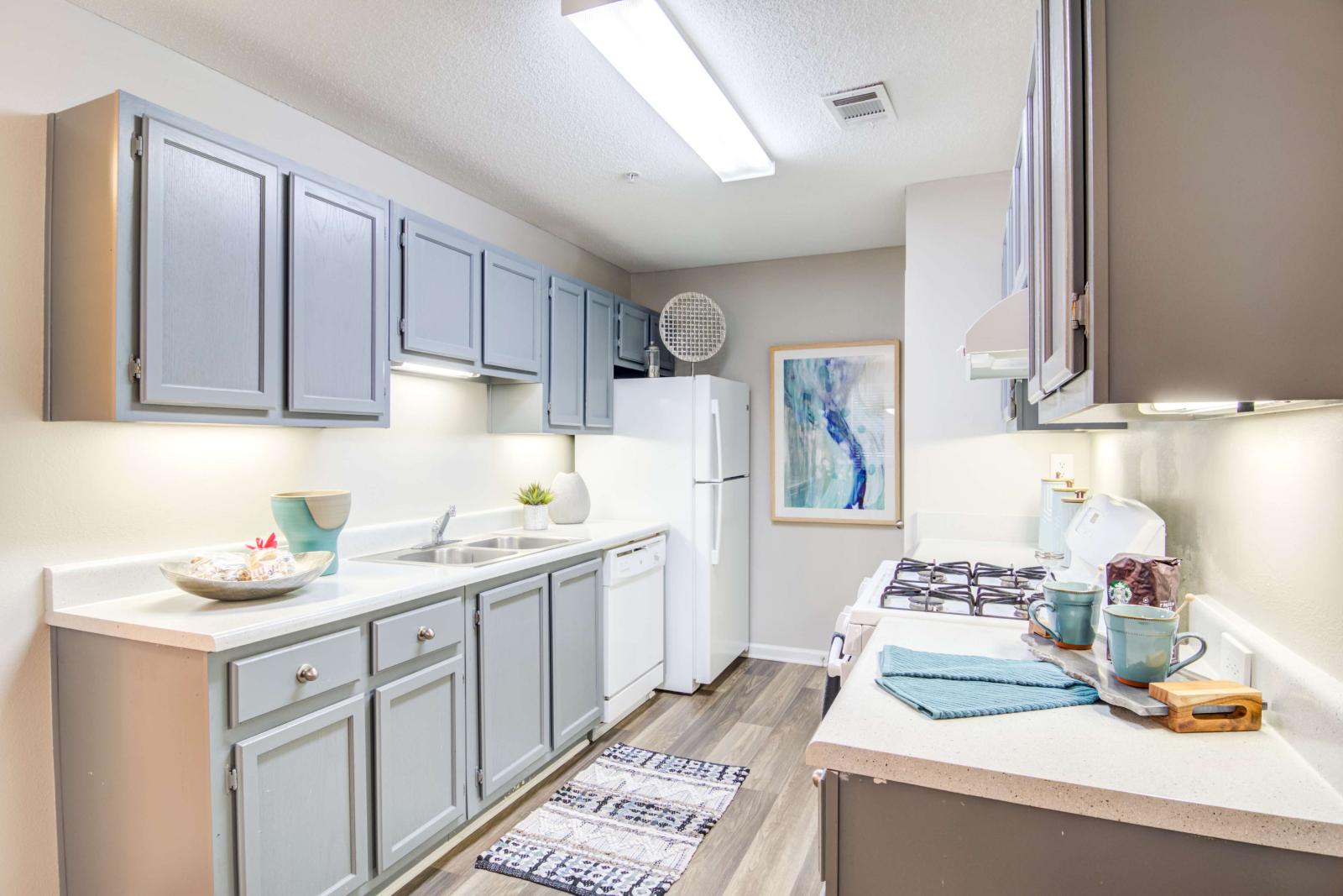 Galley-style kitchen with soft gray cabinets, white appliances, and wood-style flooring.