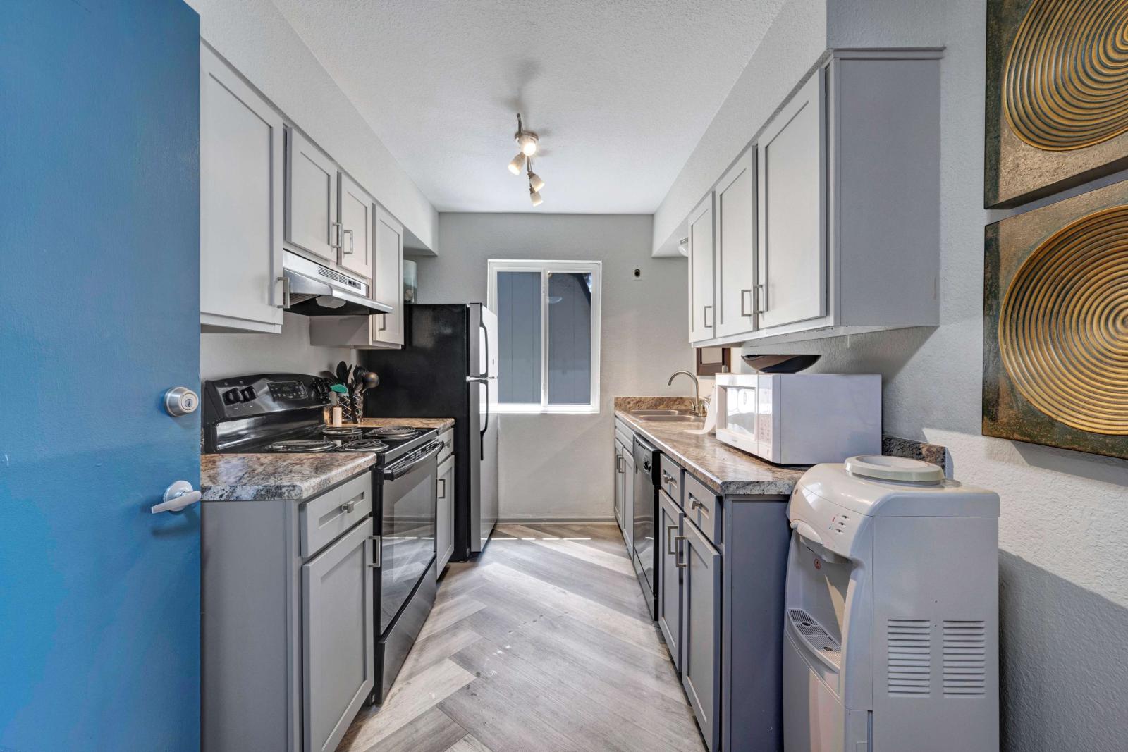 Bright kitchen with gray cabinets, black appliances, and herringbone-pattern flooring in a modern apartment.