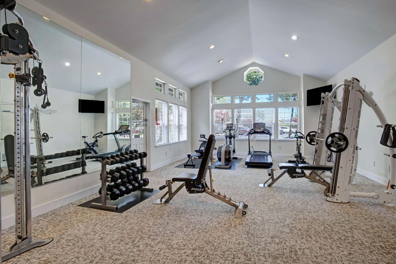 Bright, well-equipped fitness center featuring cardio machines, free weights, strength training equipment, and large windows that fill the space with natural light.