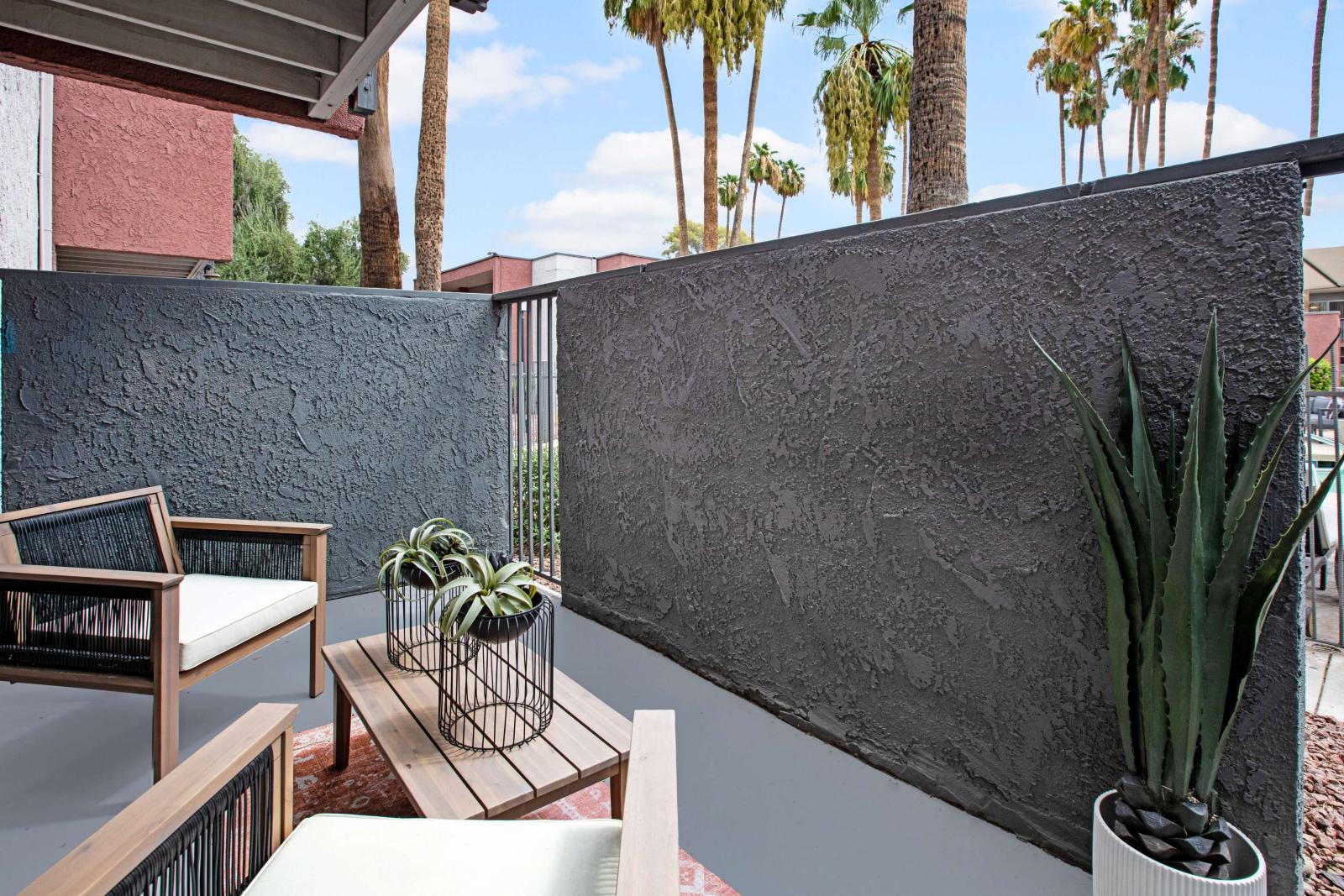 Private patio with stylish outdoor seating and potted plants, surrounded by tall palm trees and modern apartment exteriors.