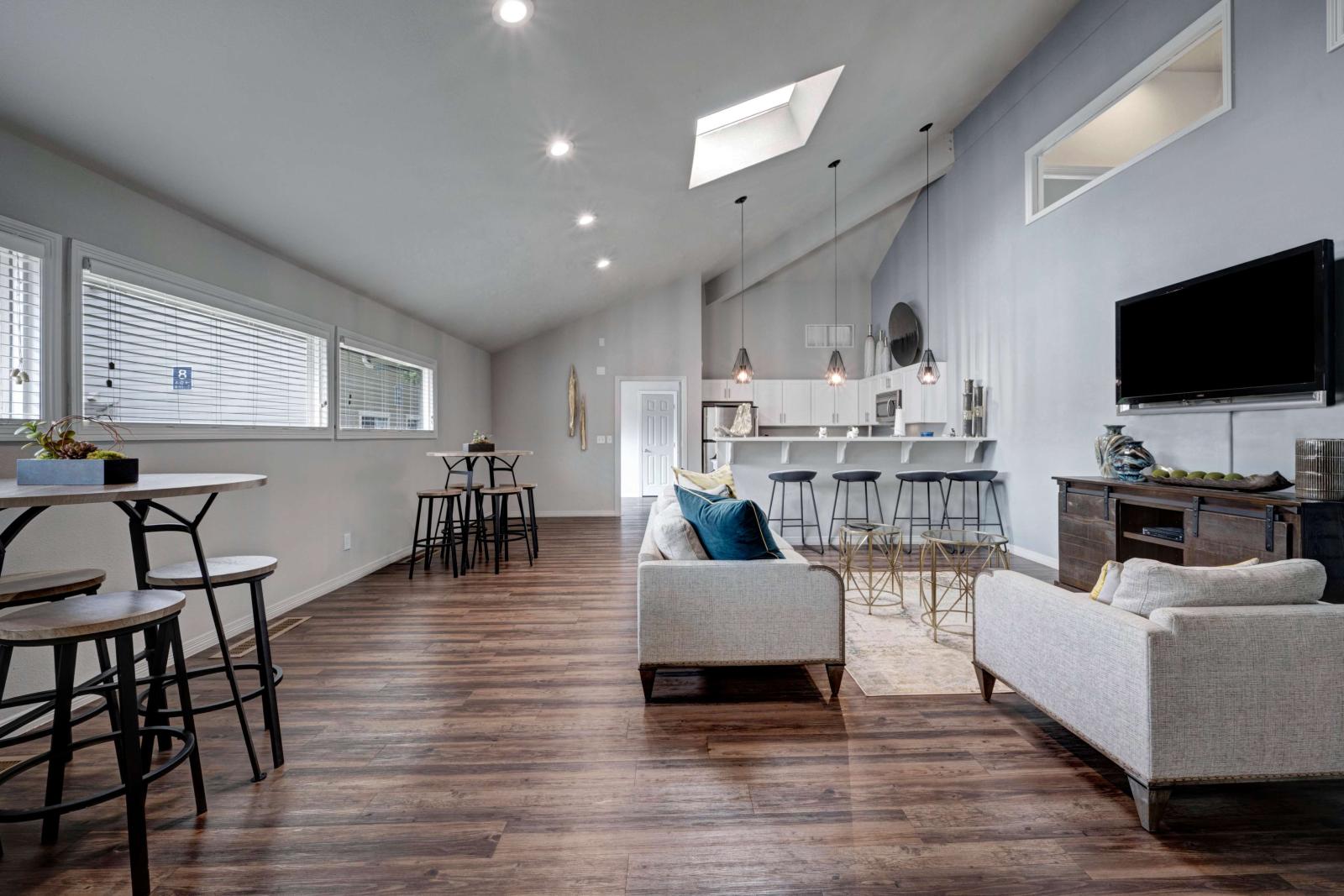 Modern resident clubhouse with vaulted ceilings, skylight, wood-style flooring, bar seating, and contemporary lounge furniture with a mounted TV and kitchen area.
