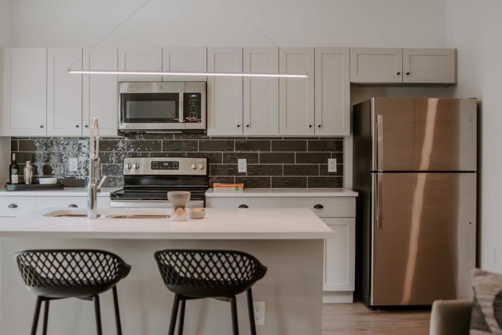 Open-concept kitchen with a spacious island, pendant lighting, and a mix of contemporary finishes, including a black tile backsplash and stainless steel appliances.