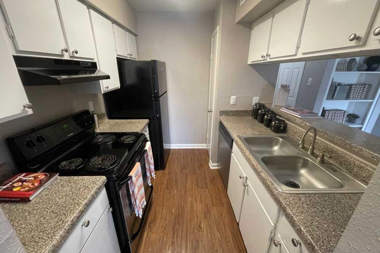 A spacious kitchen at The Oaks of Westchase Apartments featuring black appliances, sleek countertops, and ample cabinet storage.