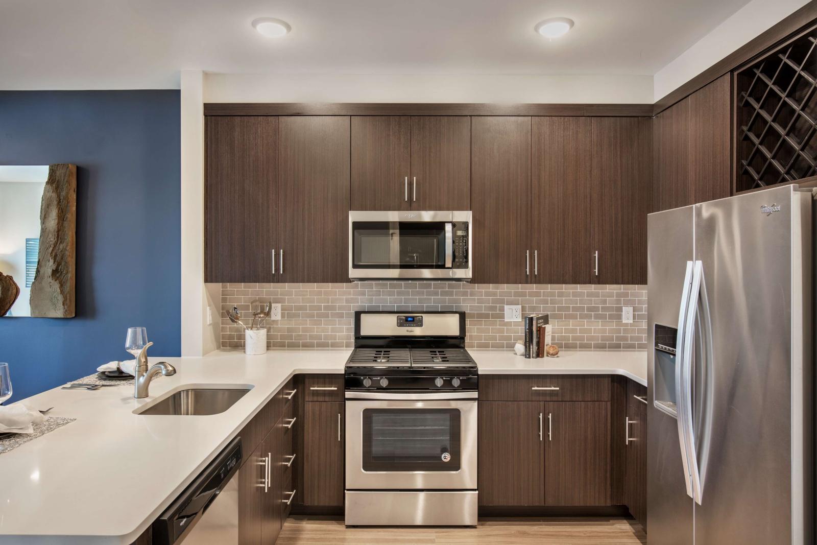 Modern kitchen featuring sleek dark wood cabinetry, stainless steel appliances including a gas range and microwave, and a built-in wine rack. The kitchen boasts a neutral subway tile backsplash and light quartz countertops, with an open layout and breakfast bar overlooking a cozy dining area. Perfect blend of contemporary style and functionality.