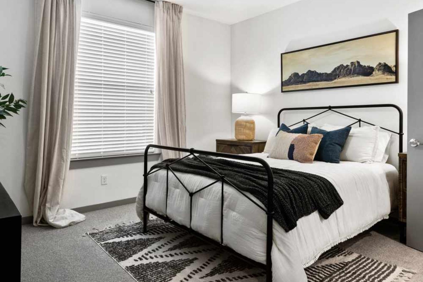 A serene bedroom with a modern metal bed frame, cozy bedding, and a large window for natural light.