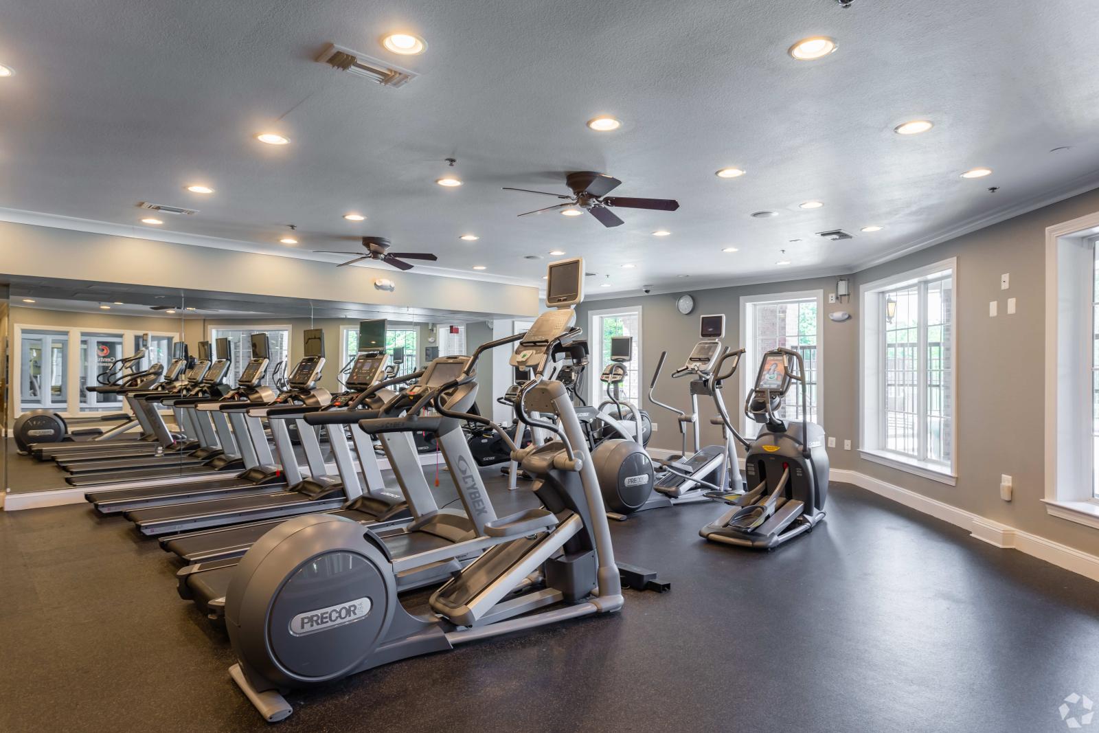 A bright and well-equipped fitness center featuring treadmills, elliptical machines, and large windows for natural light.