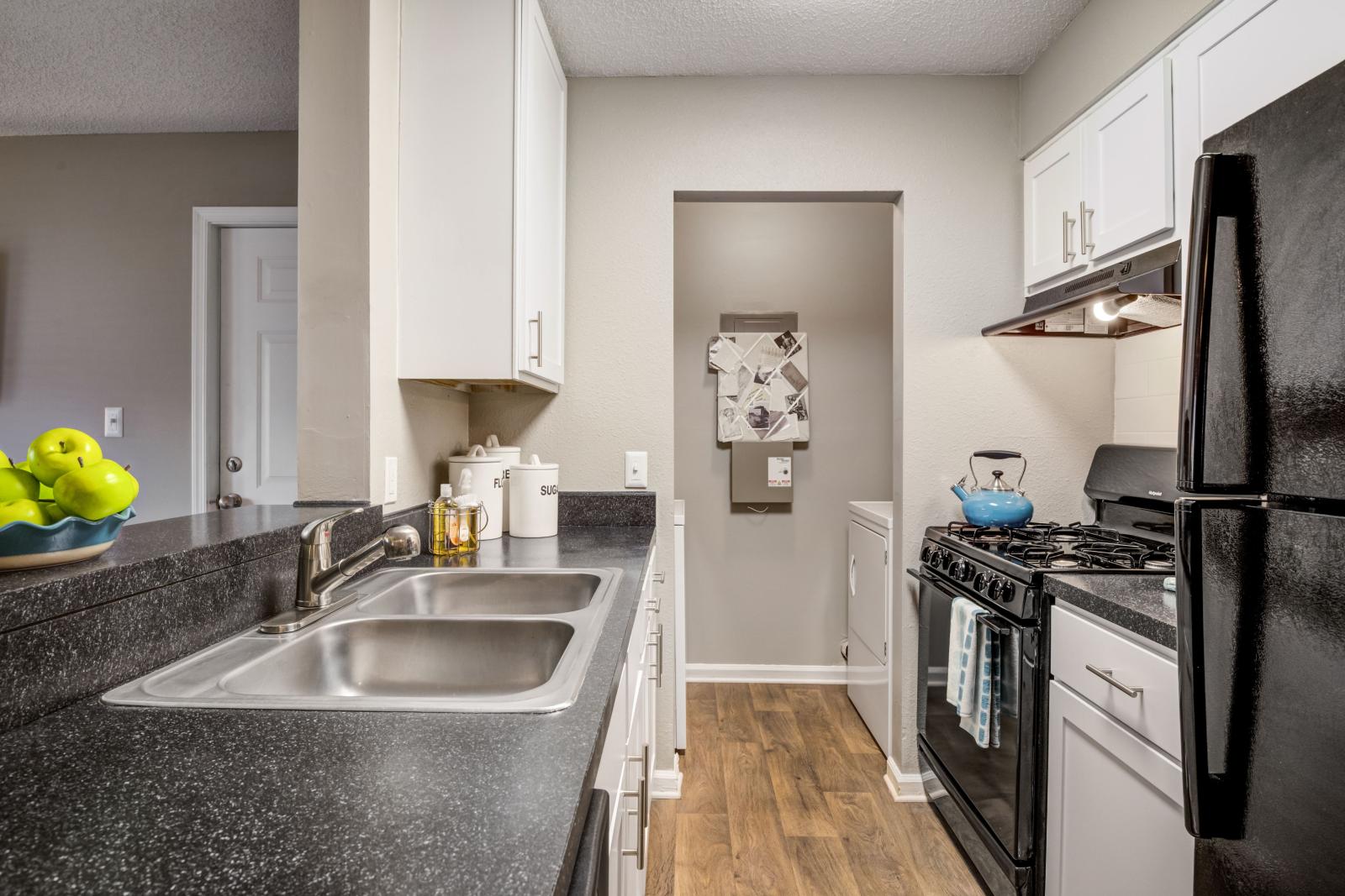 Kitchen at The Samuel with black countertops, white cabinetry, black appliances, and adjacent laundry space
